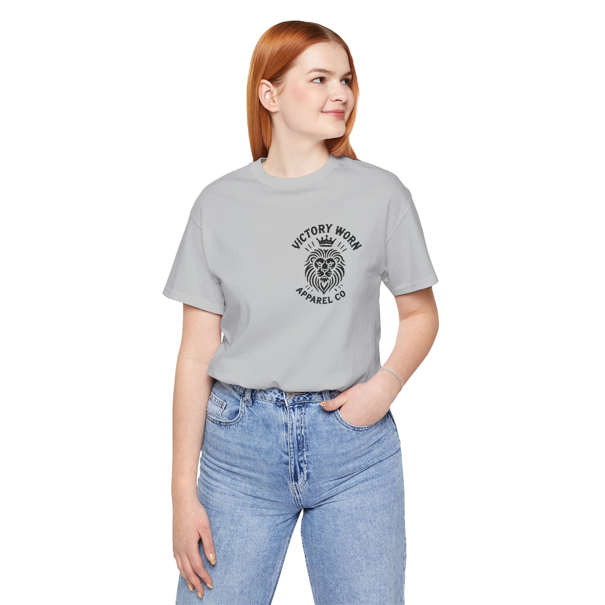 Death Defeated' T-shirt in Heather Storm, featuring the Victory Worn Apparel Co. lion logo on the front. Modeled by a woman with red hair wearing light blue jeans, looking off to the side.